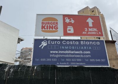Carteles publicitarios de Burger King y de la inmobiliaria Euro Costa Blanca sobre una valla en una calle de Benidorm.